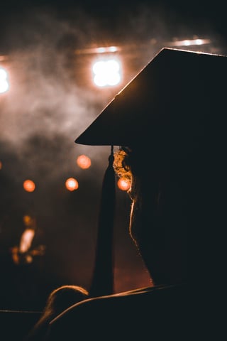 Silhouette of a graduate in a mortarboard under stage lights