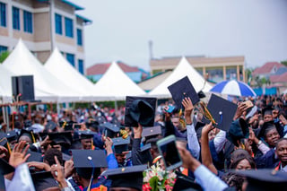 Graduates holding their caps up at an outdoor ceremony