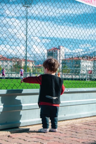 Young fan watching a soccer game through a fence