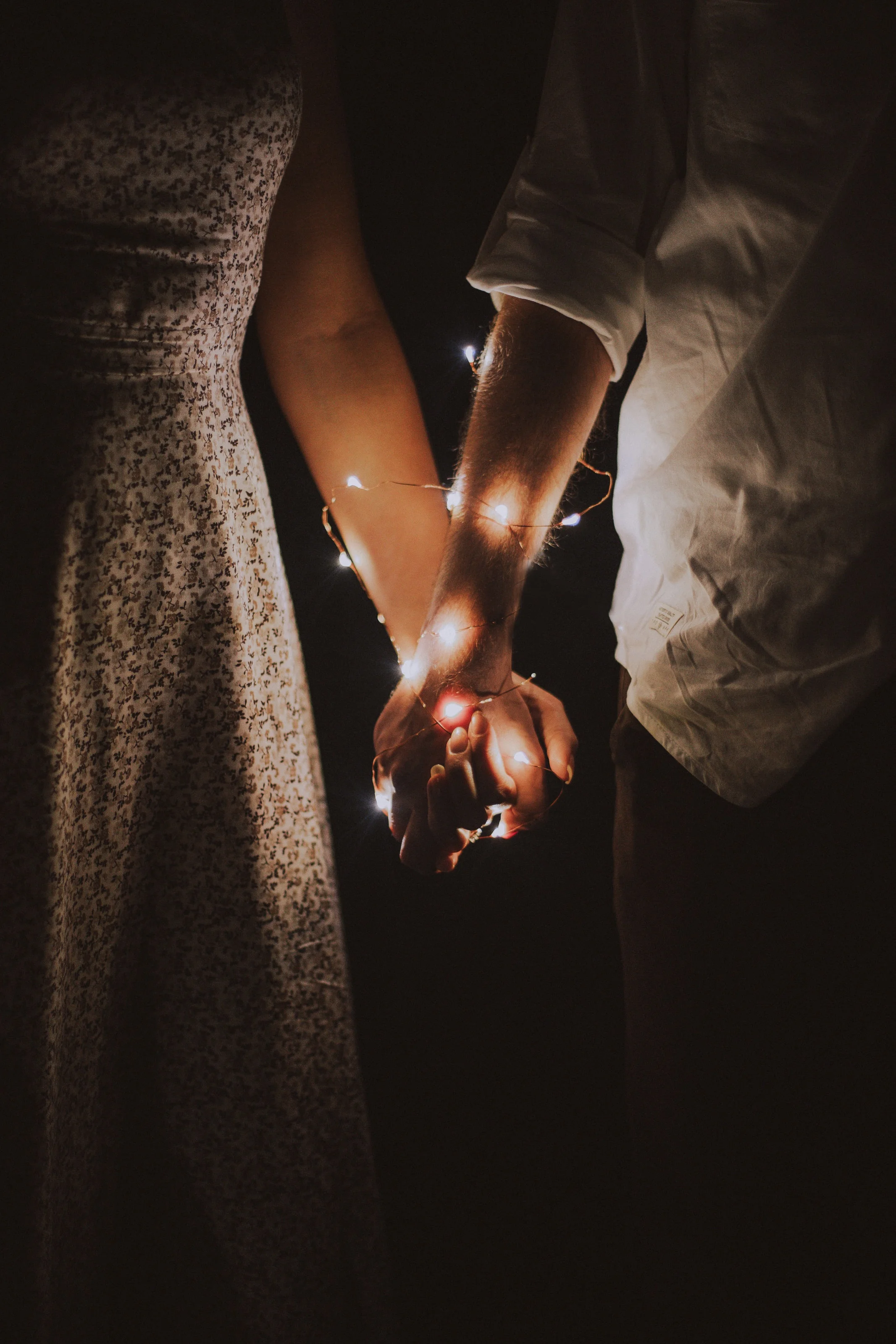 a photograph of couple holding hands with lights wrapped their hands