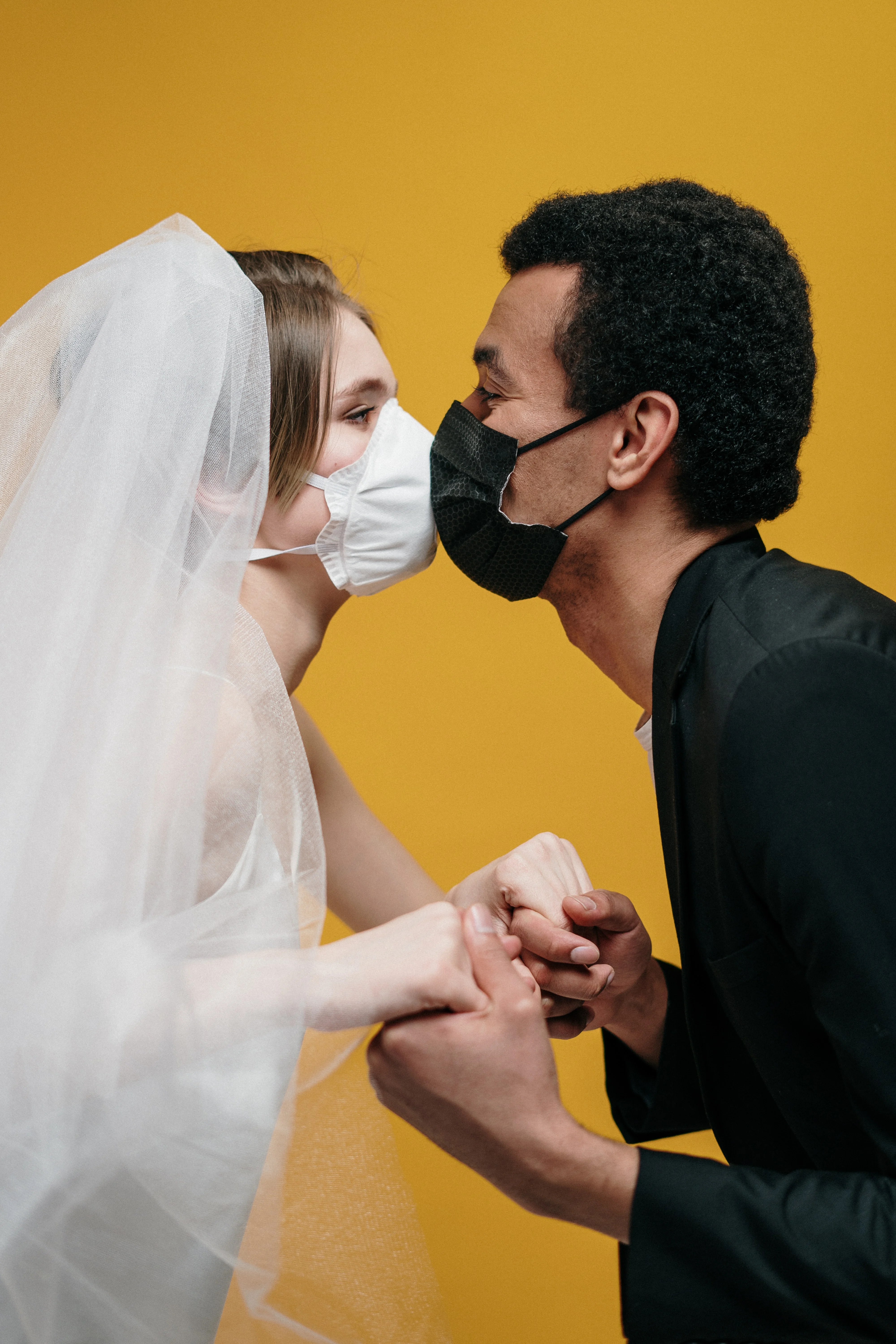 a wedding photograph of groom and bride kissing while wearing a facemask