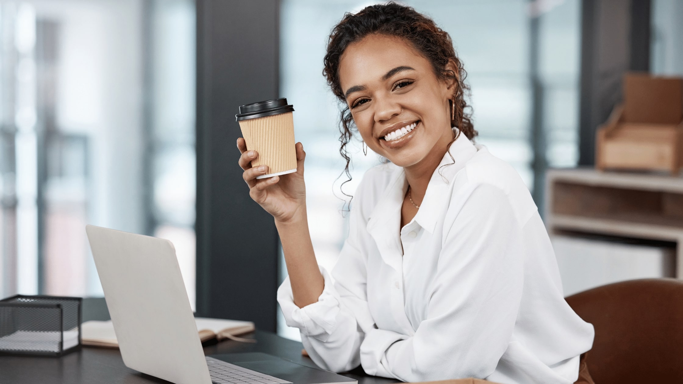 A woman with a laptop while hoding a cup of coffee